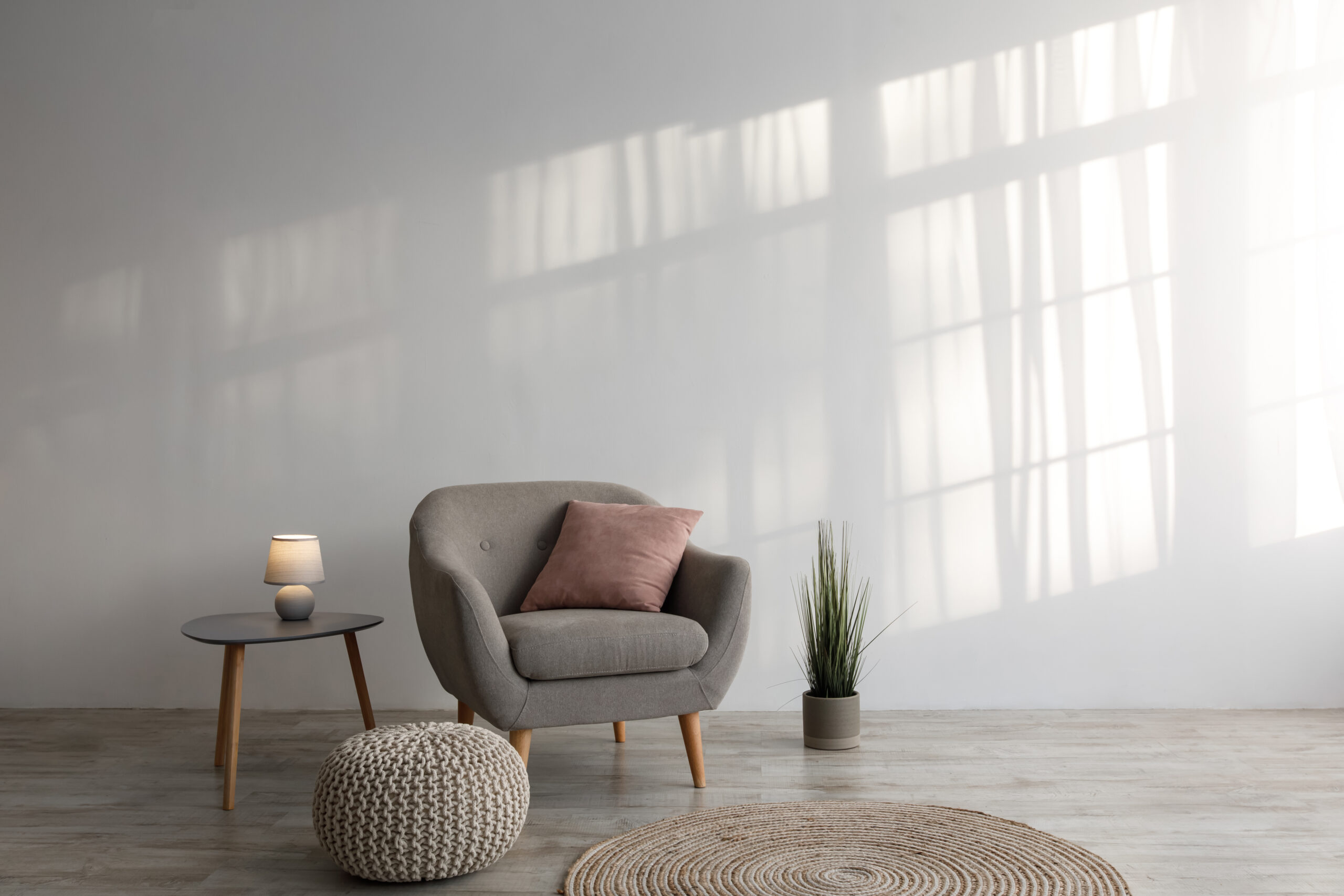 About cozy armchair with pillow, luminous lamp on table, potted plant, ottoman and round carpet